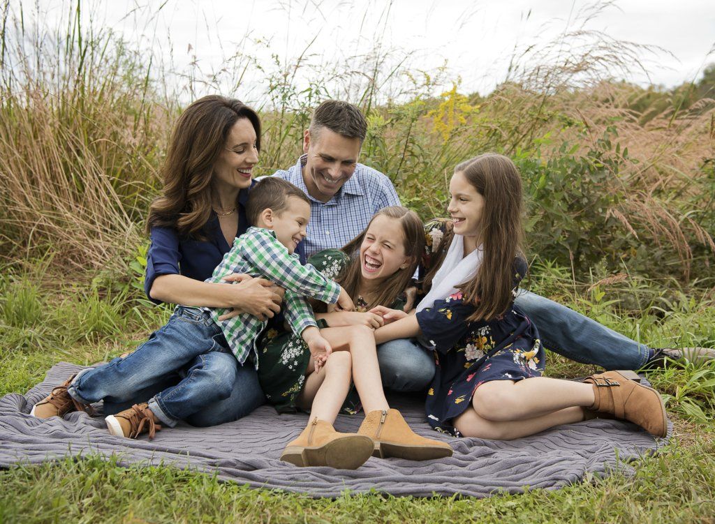 family sitting on a blanket tickling girl at the park