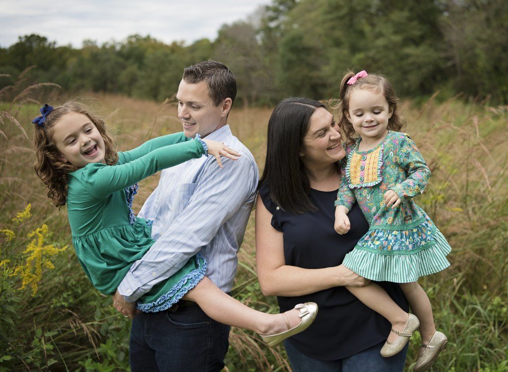 mom and dad holding daughters playing with daughters at the park