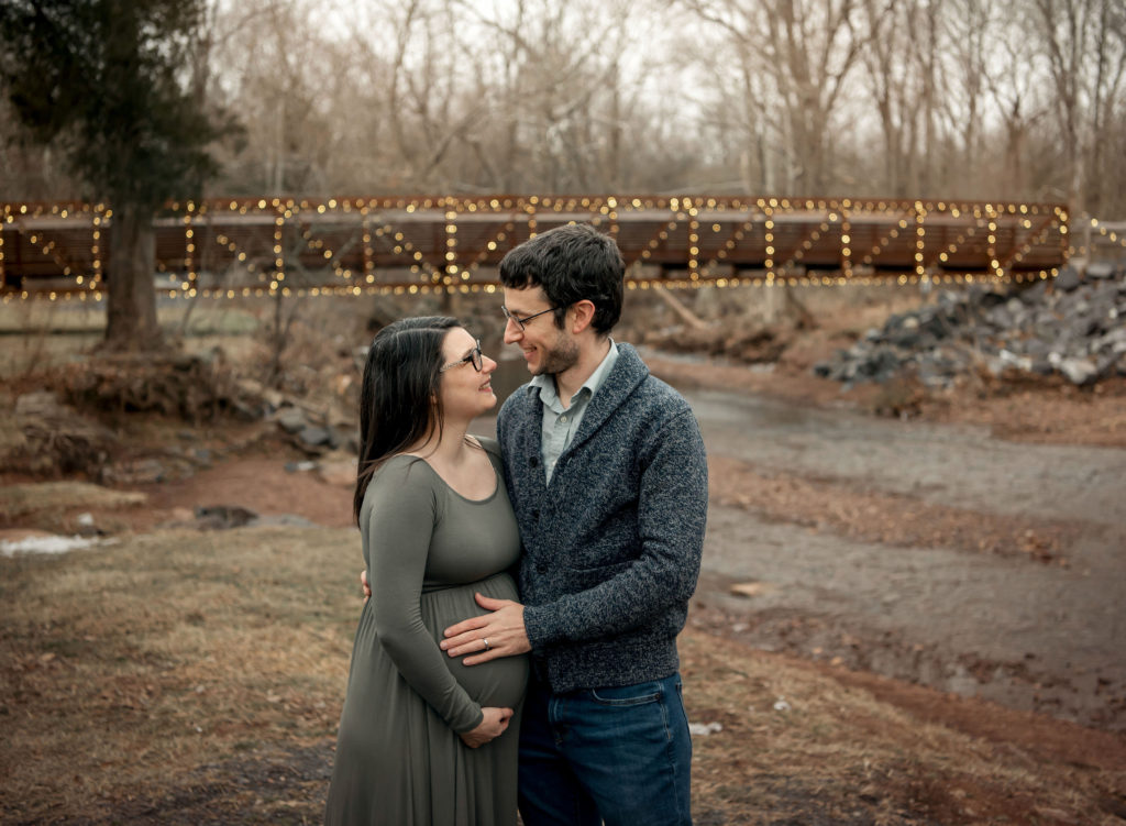 couple_maternity_portrait_session_pregnant_green_dress_couple_ creek_bridge_lights_fischers_park_Lansdale
