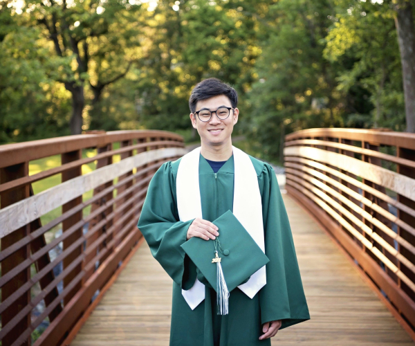Methacton High School Senior holding green cap and wearing gown standing on bridge at Fischers Park Lansdale
