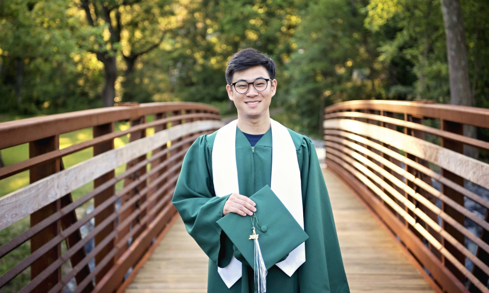 Methacton High School Senior holding green cap and wearing gown standing on bridge at Fischers Park Lansdale