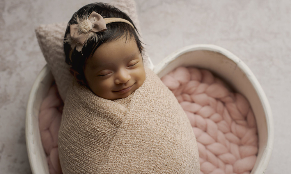 A newborn baby girl wearing pink in heart bowl is smiling Lansdale Family and Newborn Photographer