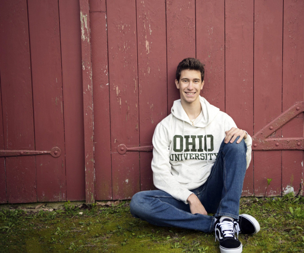 High School Senior sitting in front of red barn wearing Ohio University shirt at Highland Mansions in Ft. Washington Lansdale family and newborn photographer