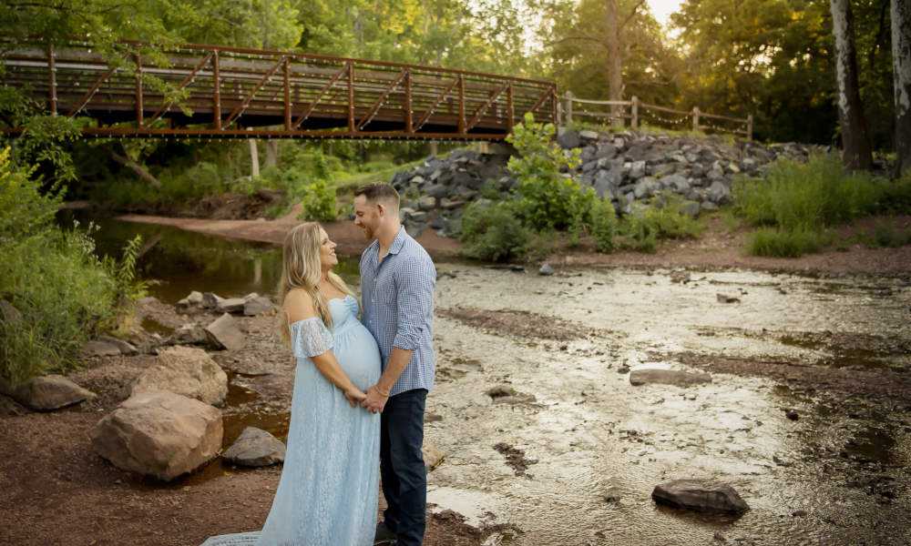 Husband holding the hand of his pregnant wife while looking at each other at fischers park in lansdale
