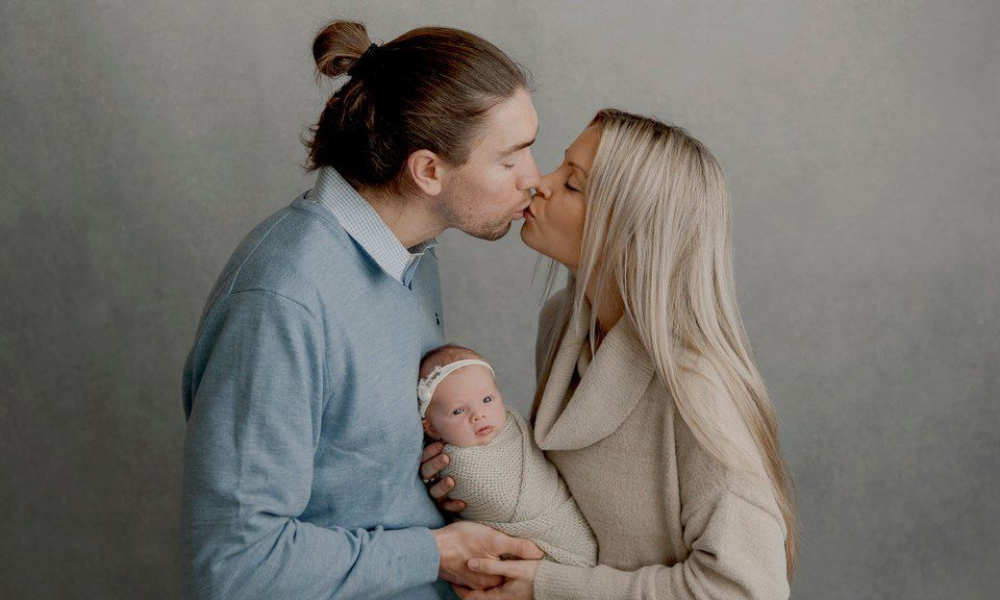 Mom and Dad holding in lap a newborn baby while kissing