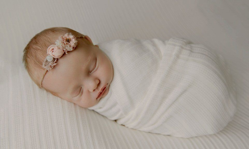Newborn baby in white wrap and wearing flower hairband